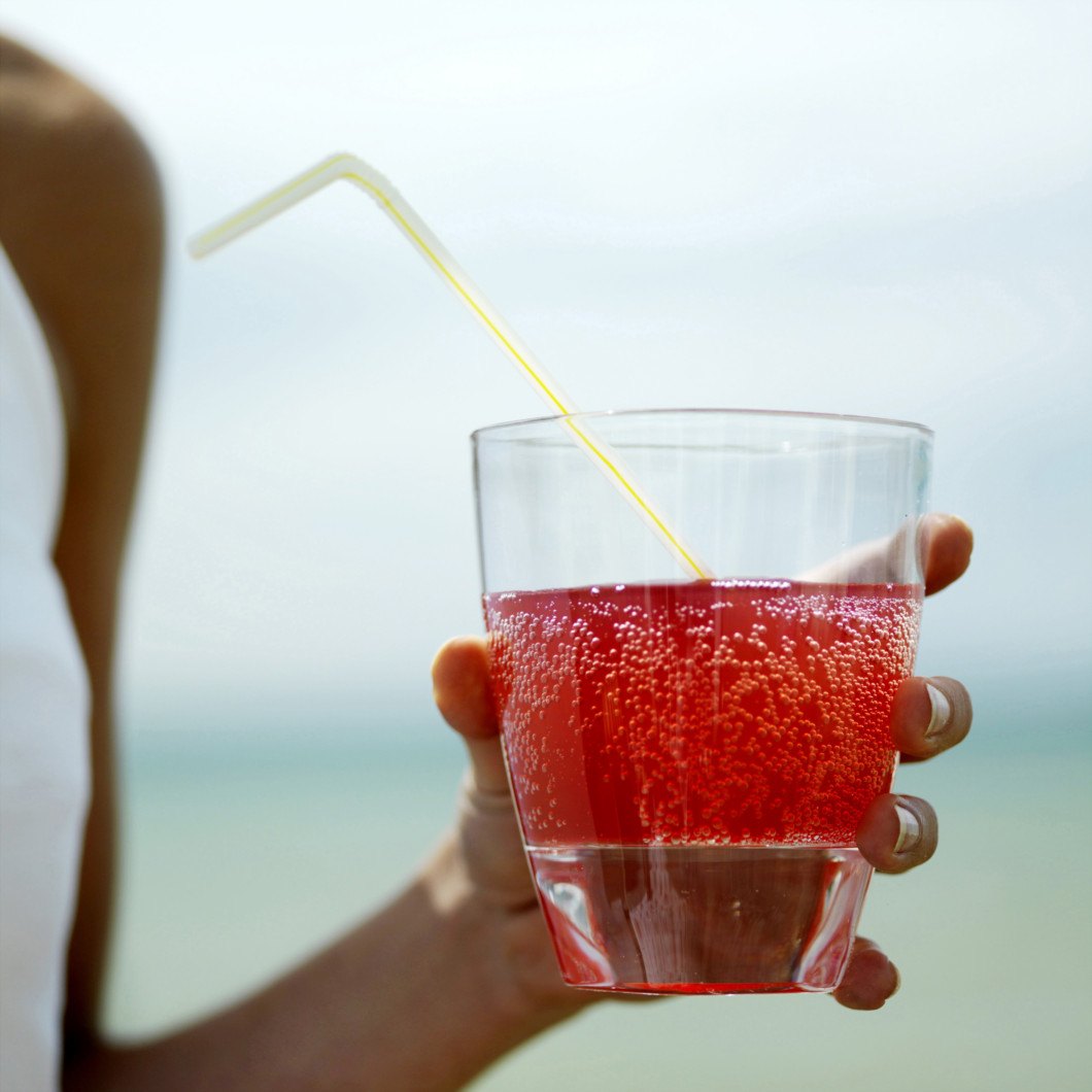 A lady holding a red sugary fizzy drink with a straw in